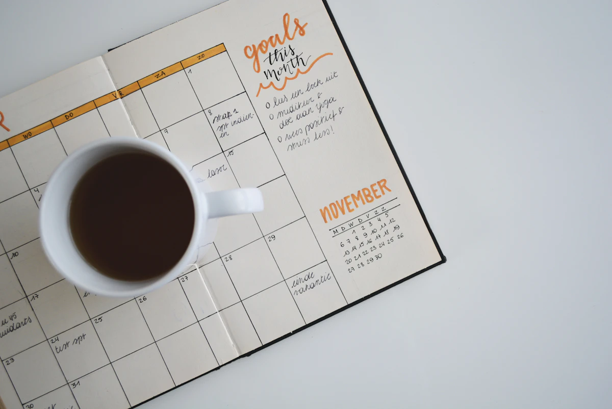 Coachingsessie aan een lichte werktafel met notitieboek en koffie